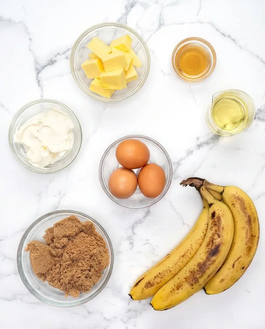 Banana-Bread-Ingredients-1a.jpg Overhead view of baking ingredients arranged on marble, labeled with sour cream, butter, sugar, eggs, vanilla, oil, and bananas.