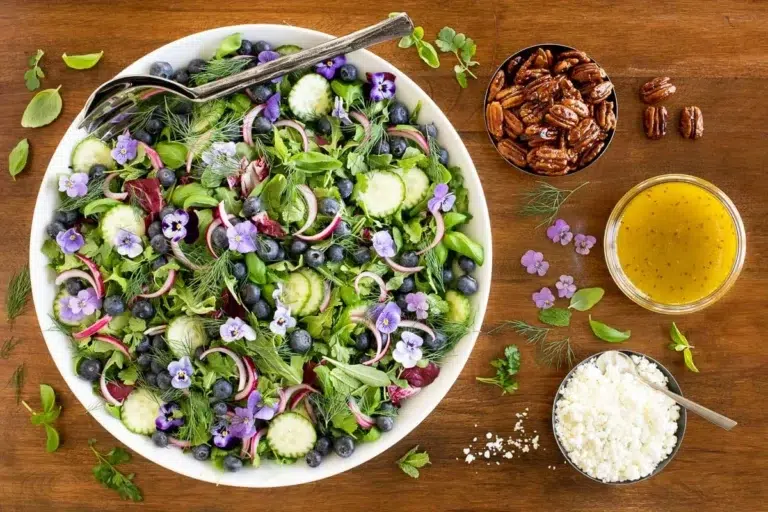 overhead view of a white serving bowl of Blueberry Arugula Herb Salad on a wood table