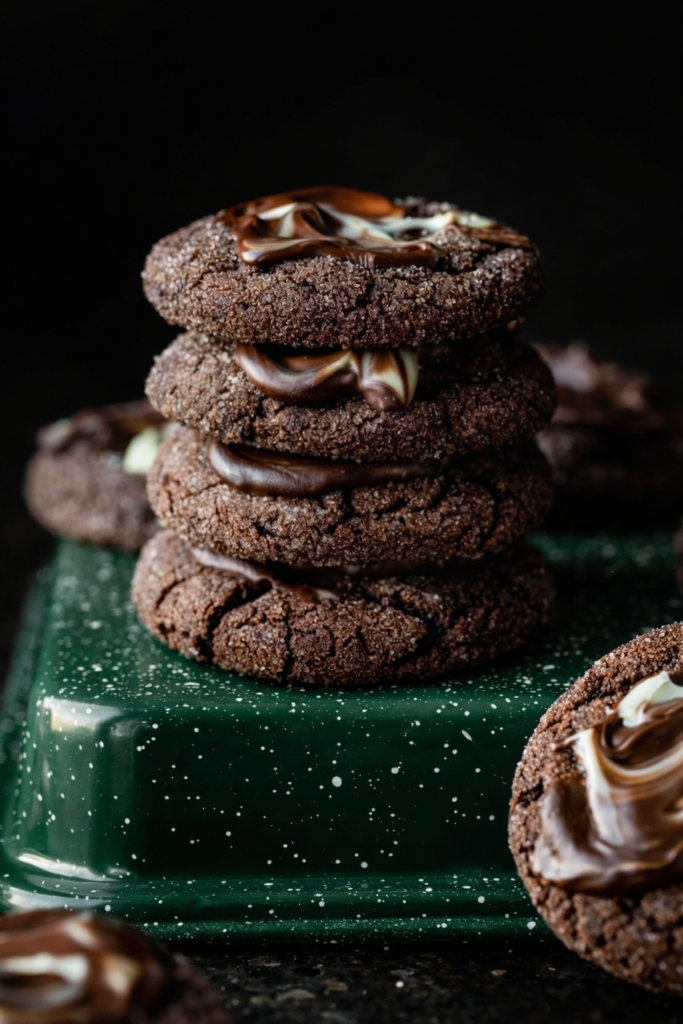 Stack of four dark chocolate cookies with marbled cream filling on a green speckled stand.