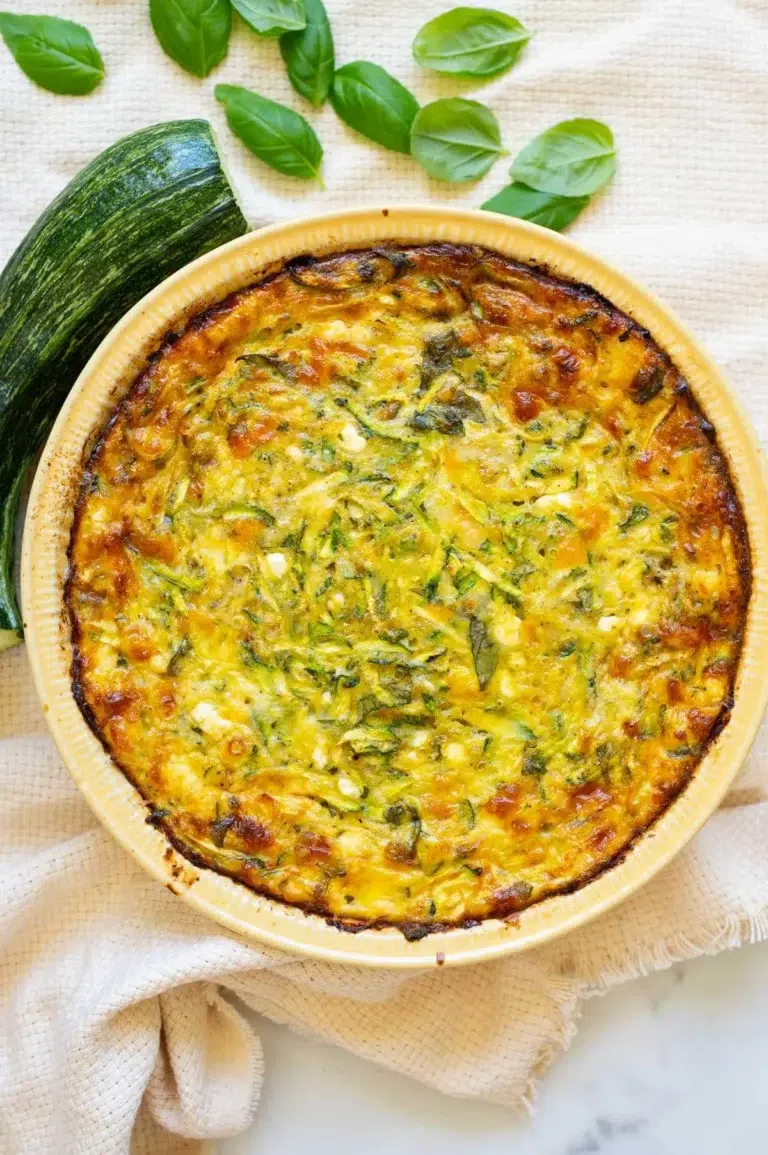 Crustless cottage cheese zucchini quiche in a pie plate. Zucchini and basil on a counter.