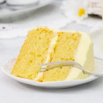 Yellow cake with lemon cream cheese frosting on a white plate with a fork.