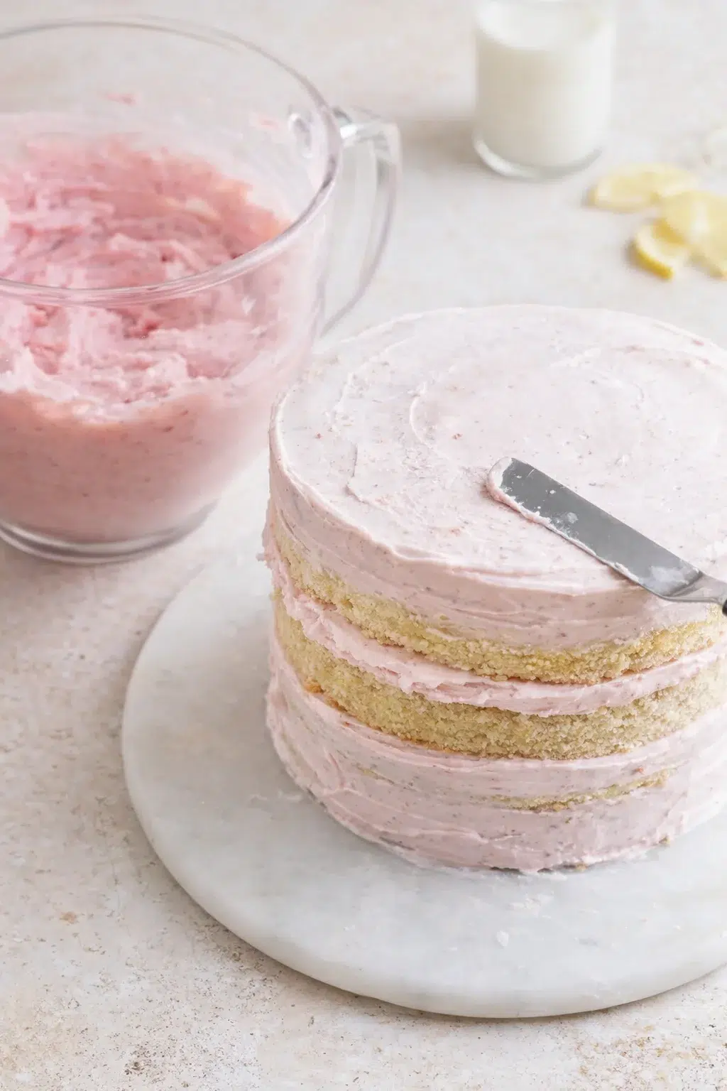 step-process-placeholder-13-16.png First cake layer on board while pink strawberry buttercream is spread, then crumb-coated and chilled.