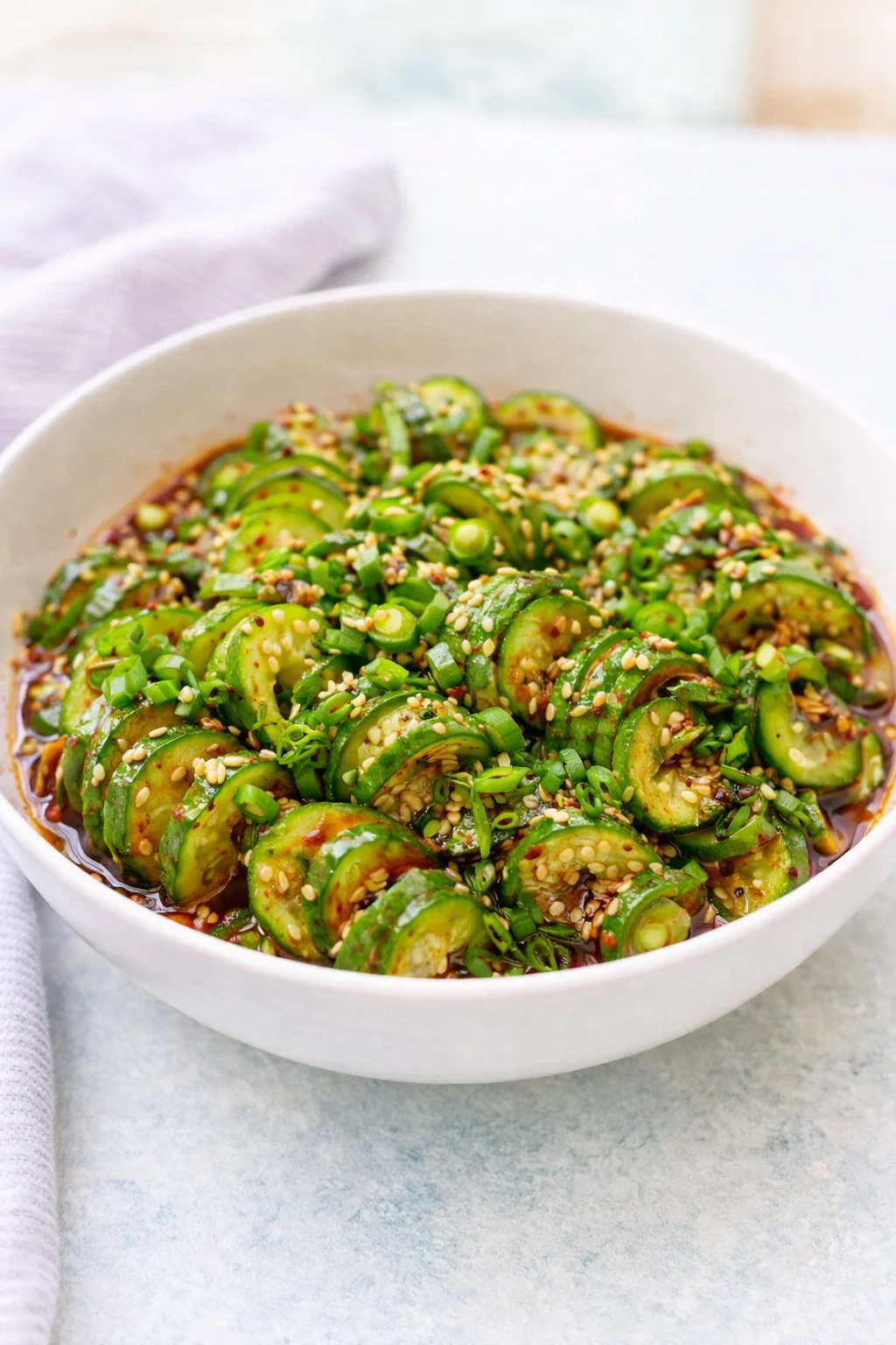 Cucumber salad tossed in a bowl, glistening with dressing and garnished with sesame seeds and scallions.
