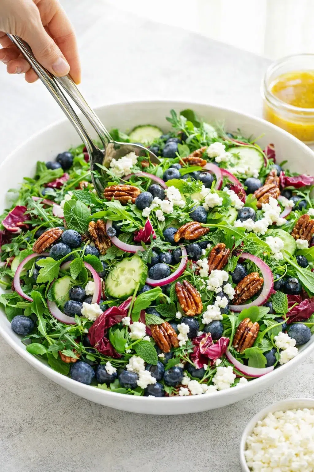 Large bowl with arugula, herbs, cucumbers, blueberries, pickled onions, candied pecans, goat cheese