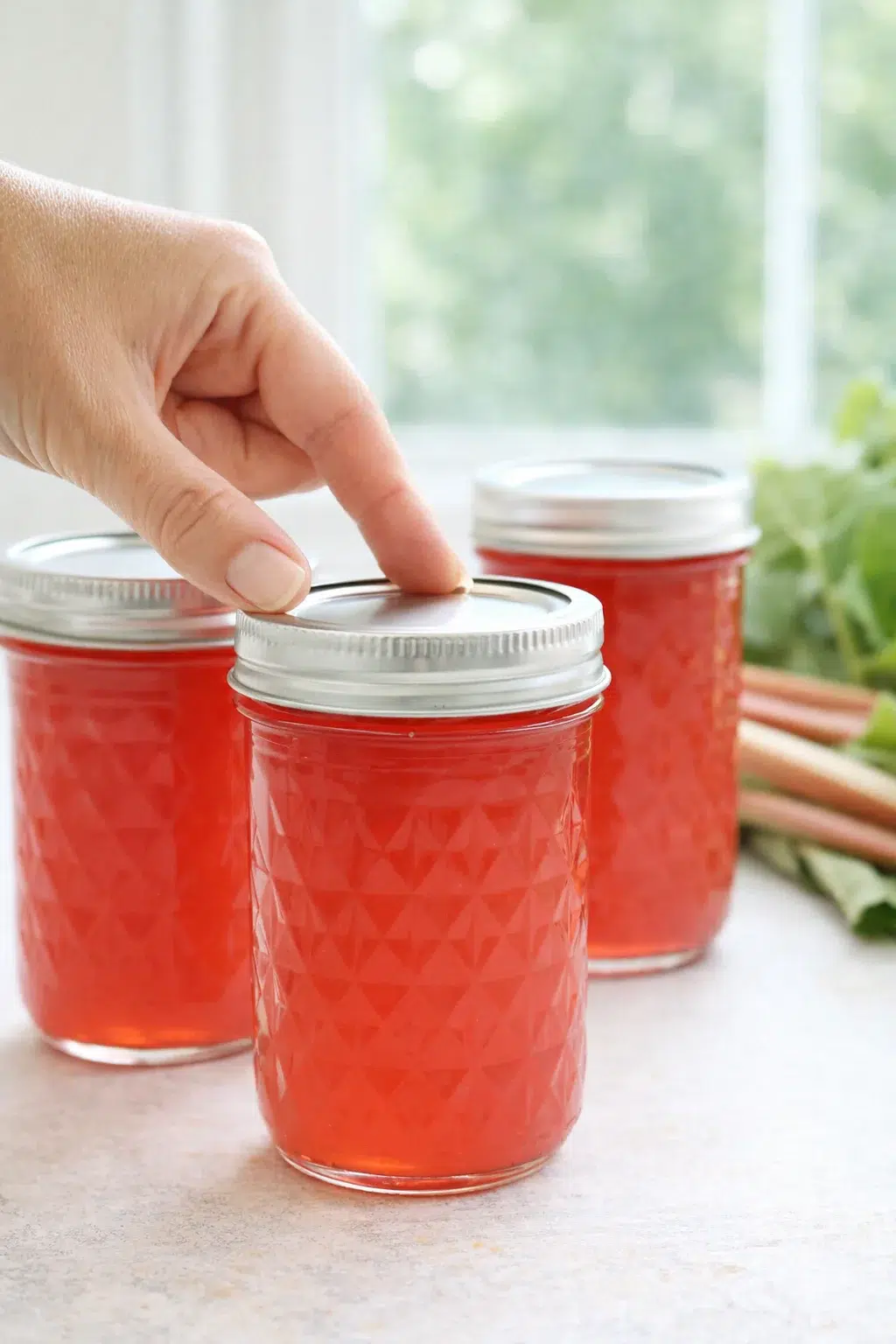 step-process-placeholder-13-13.png Jars of rhubarb concentrate cooling on a towel, lids appearing concave to indicate sealed jars