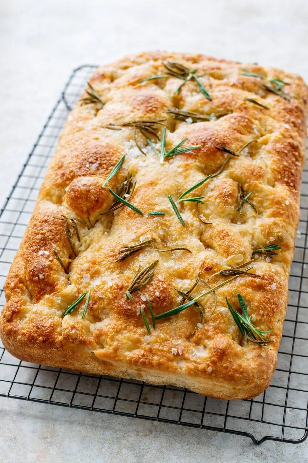 Focaccia cooling in pan before being lifted onto a wire rack to finish cooling.