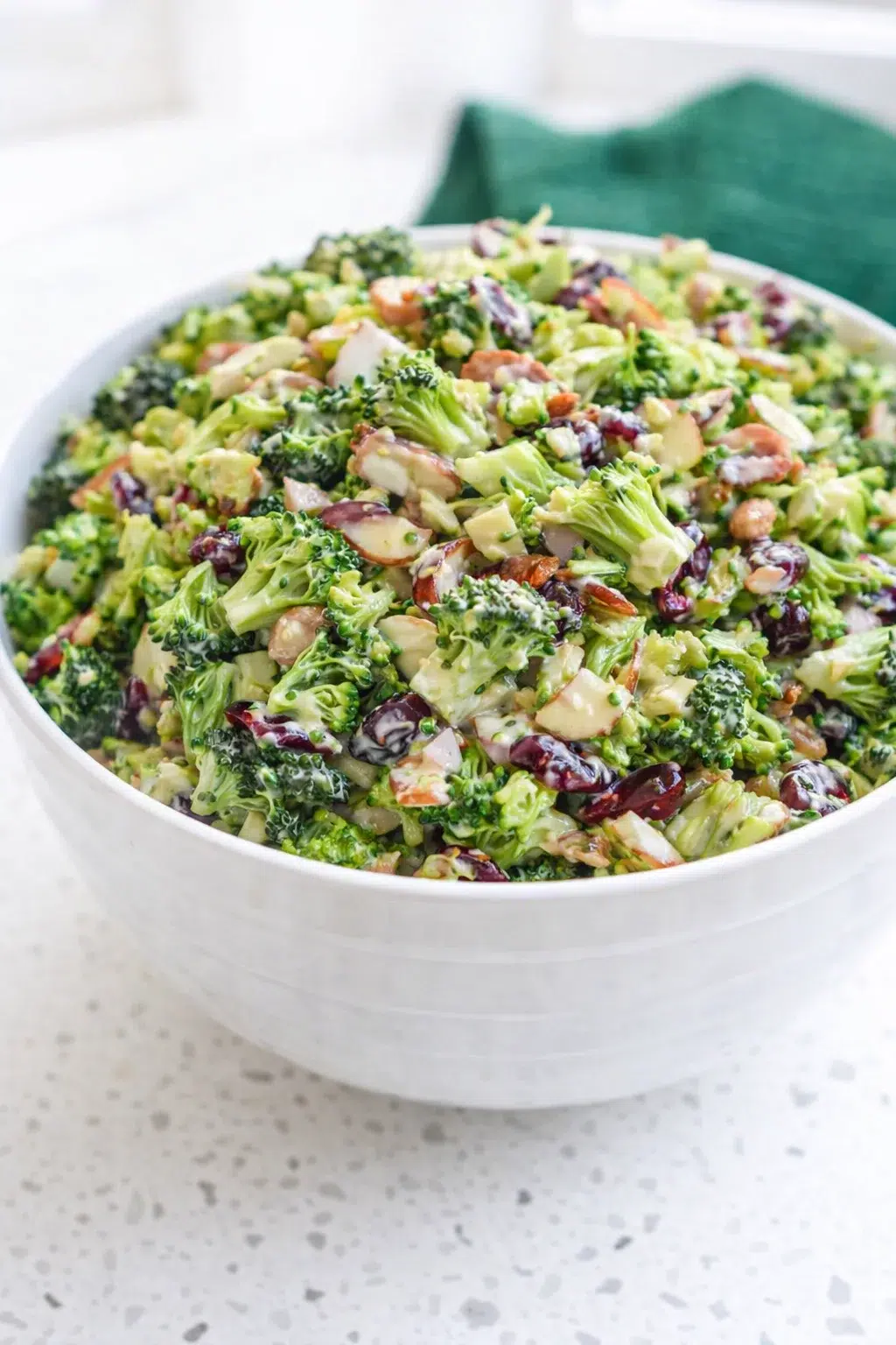 Hands using tongs to toss chilled broccoli salad just before serving.
