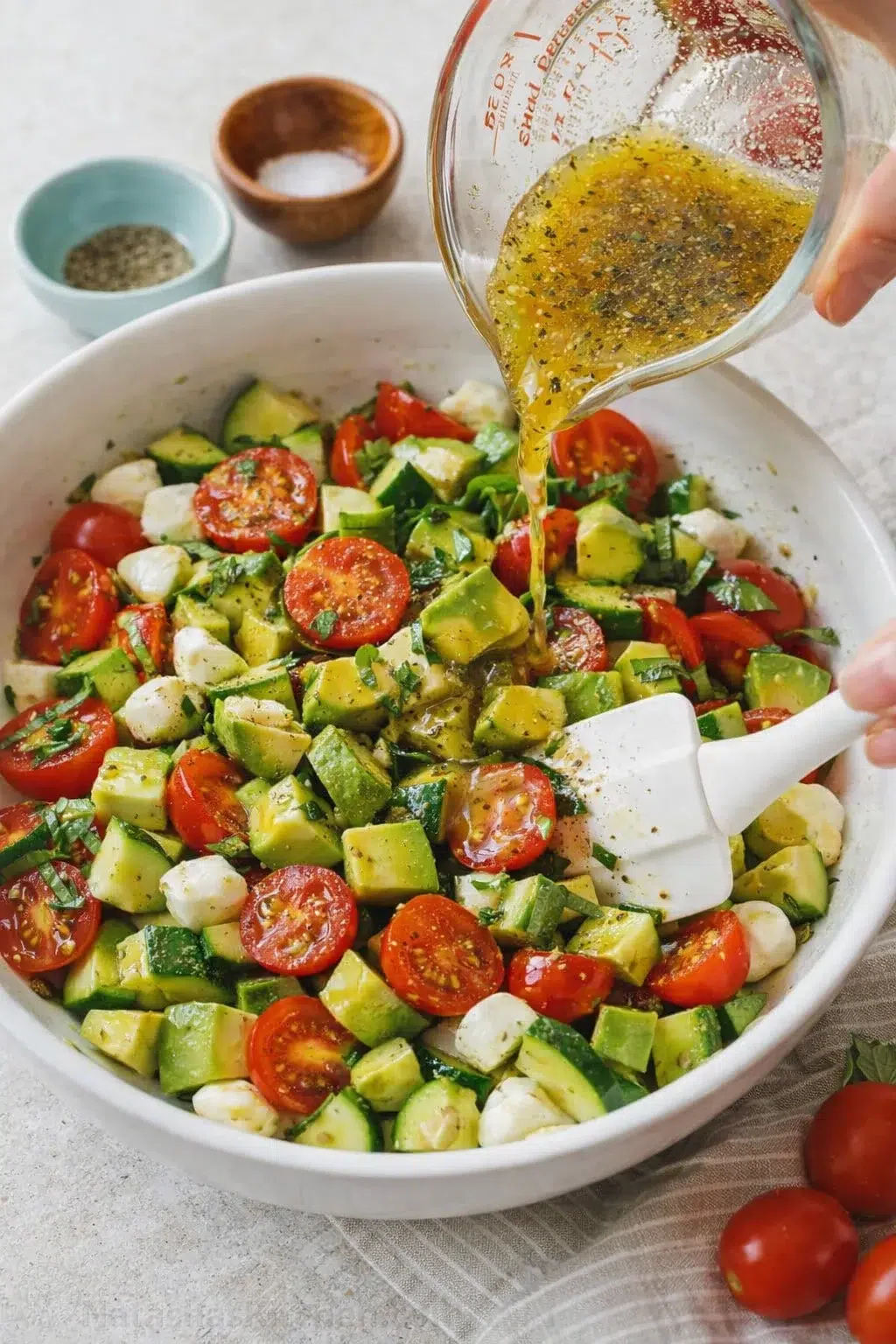 Dressing being poured over salad as avocado added, and salad gently tossed with a spatula.