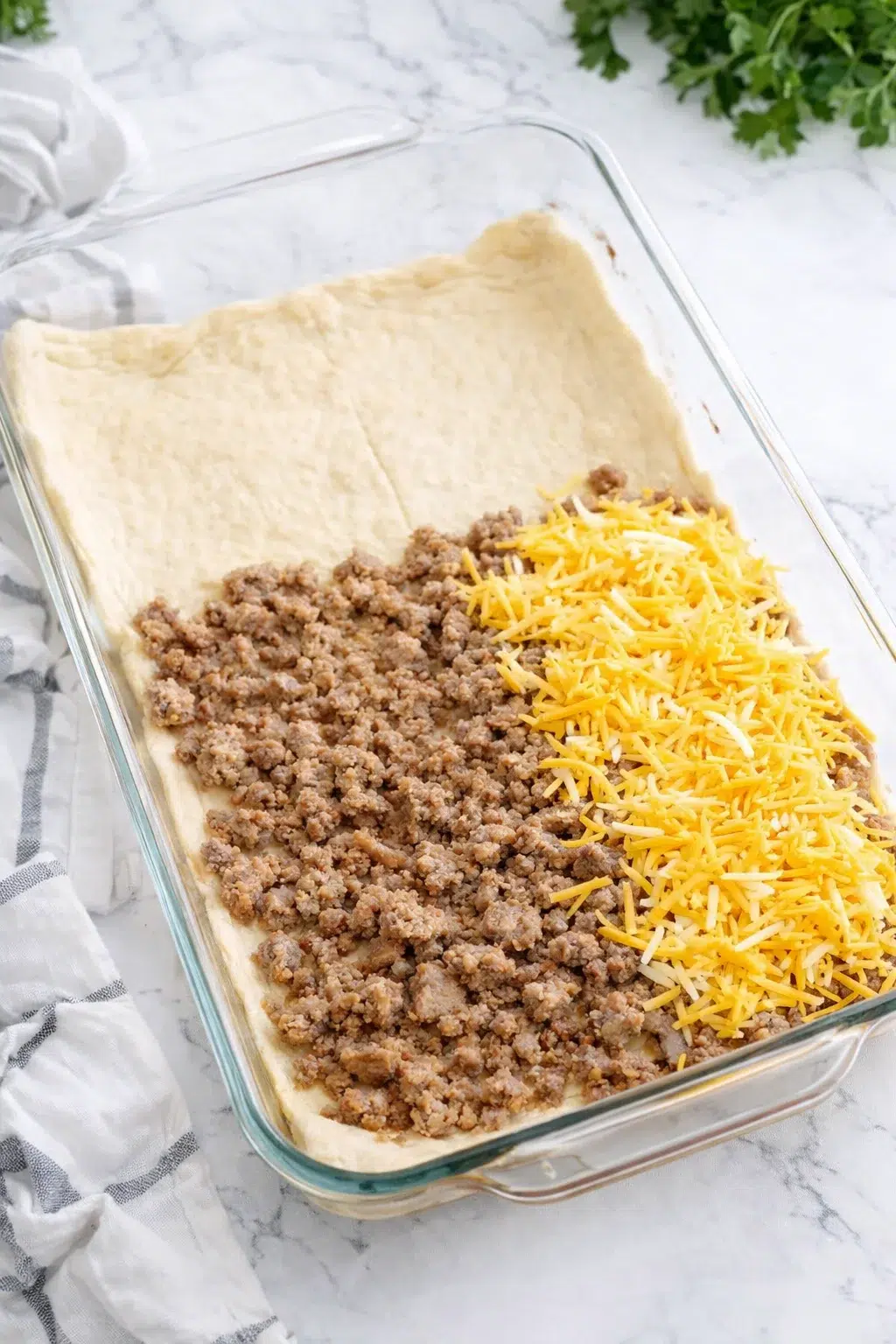 step-process-placeholder-5-8.png Hands pressing crescent roll dough into baking dish while sausage and cheese are spread evenly.
