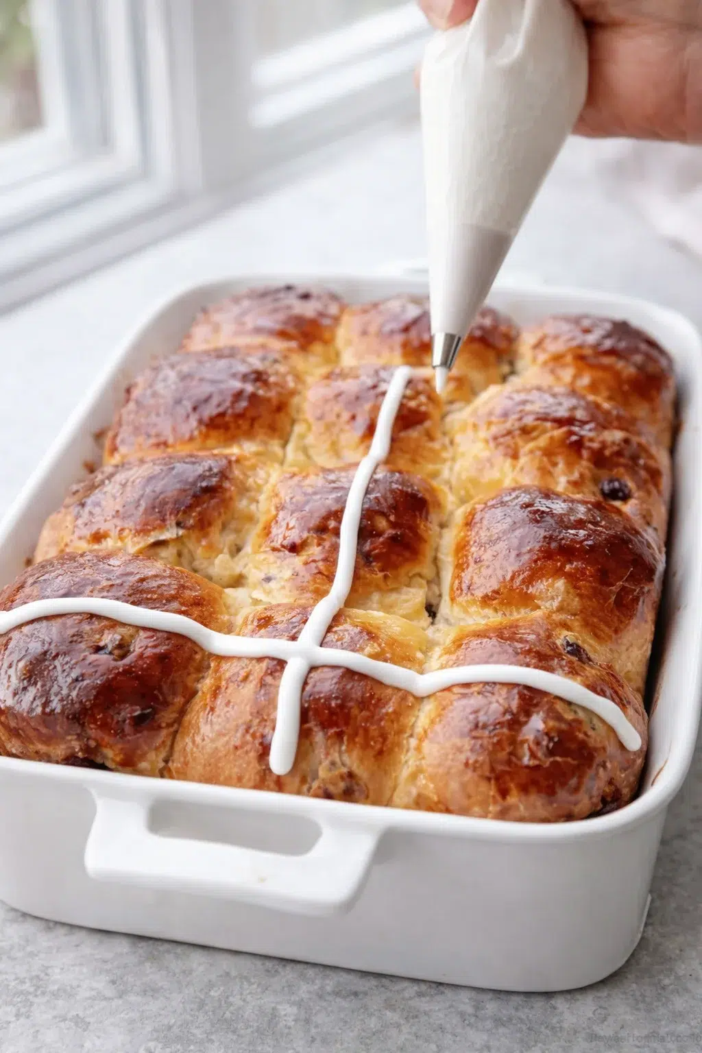 step-process-placeholder-13-13.png Thick royal icing being piped into neat crosses across cooled buns, holding defined ridges.