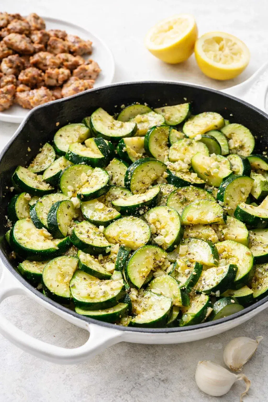 step-process-placeholder-9-12.png Cooked chicken resting on plate while zucchini cooks in skillet, garlic added and sizzling.