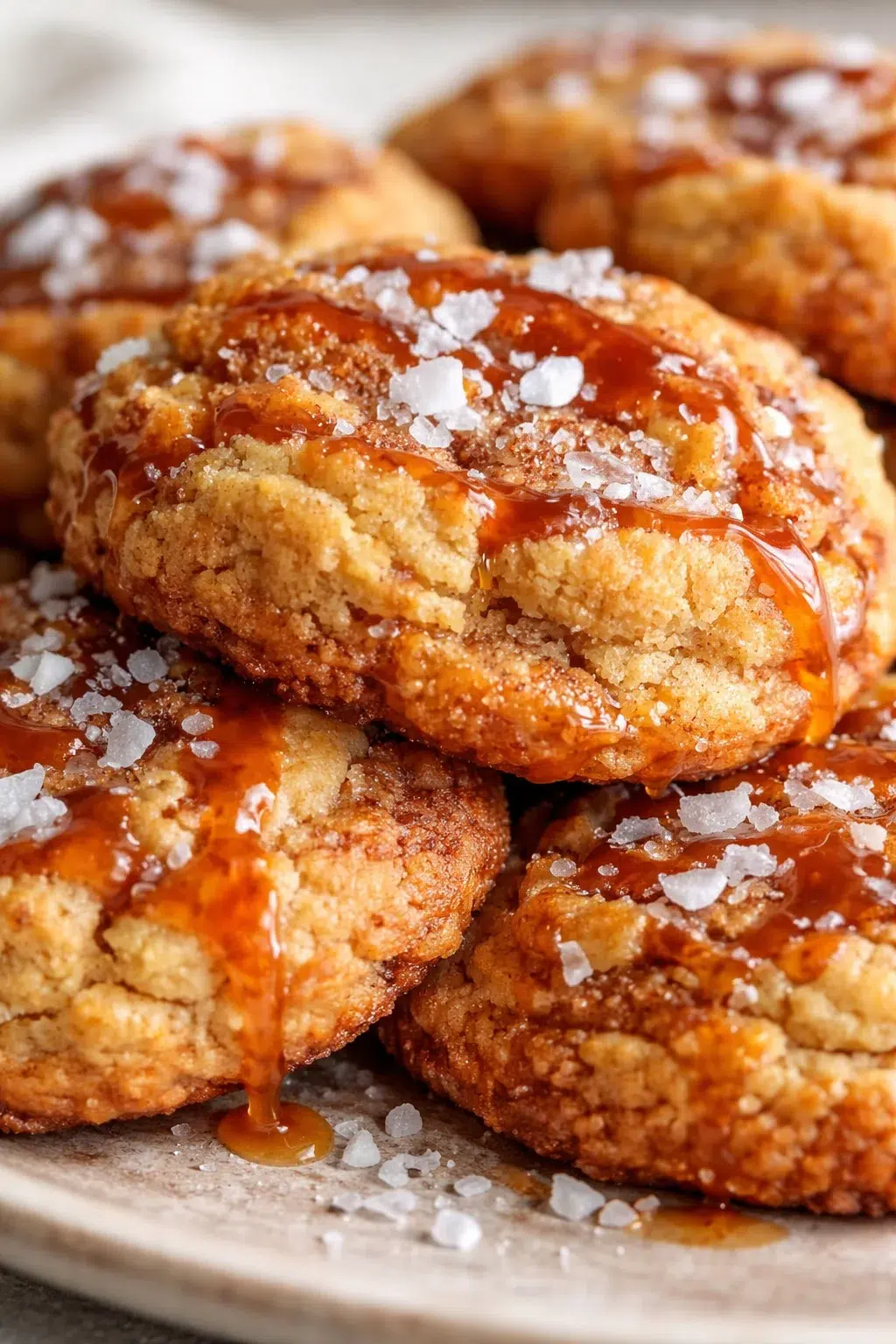 Close-up of caramel-drizzled cookies topped with flaky sea salt on a plate.