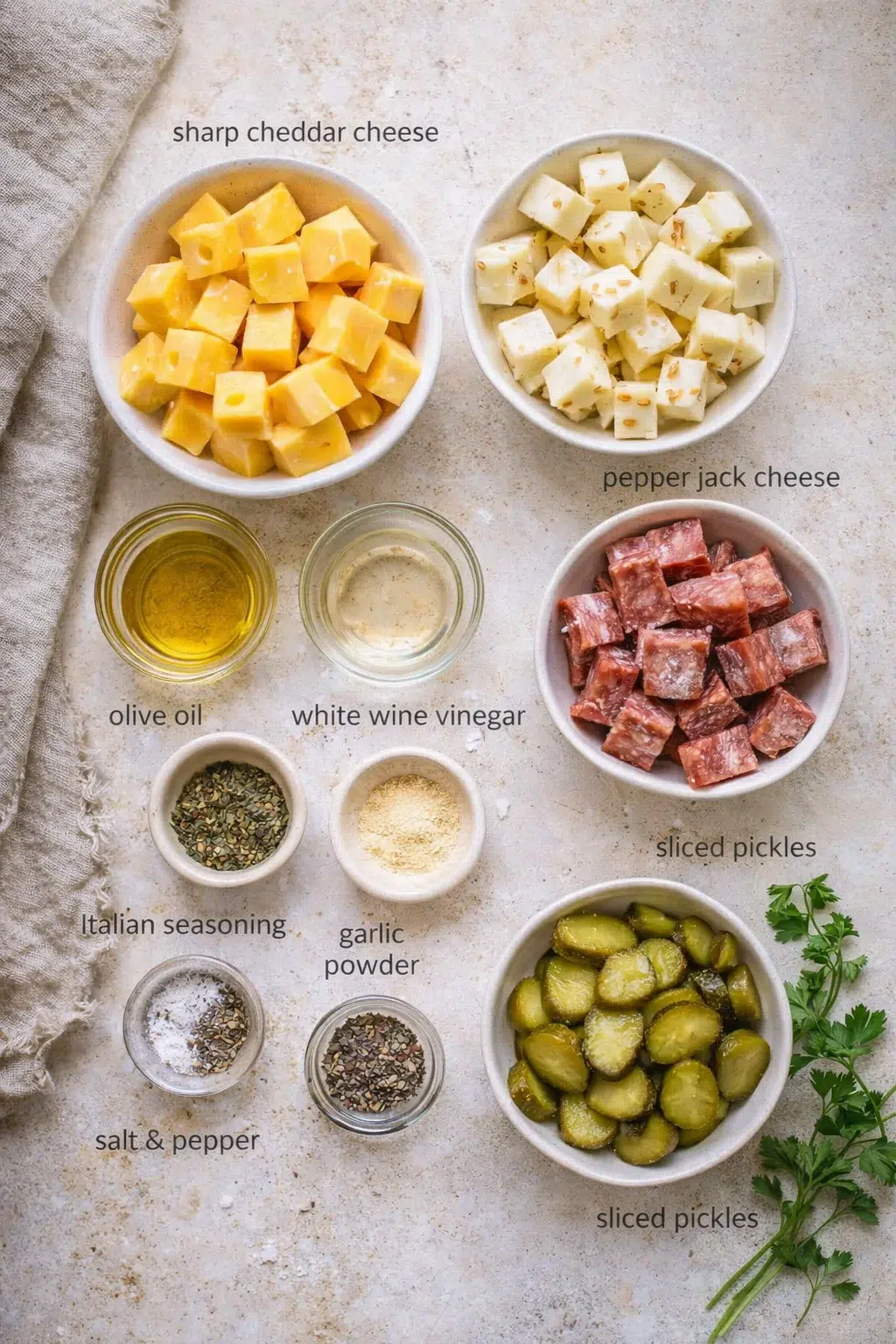 Top-down view of prep ingredients: cheddar cubes, pepper jack cheese, sliced pickles, olive oil, white wine vinegar, and spices.