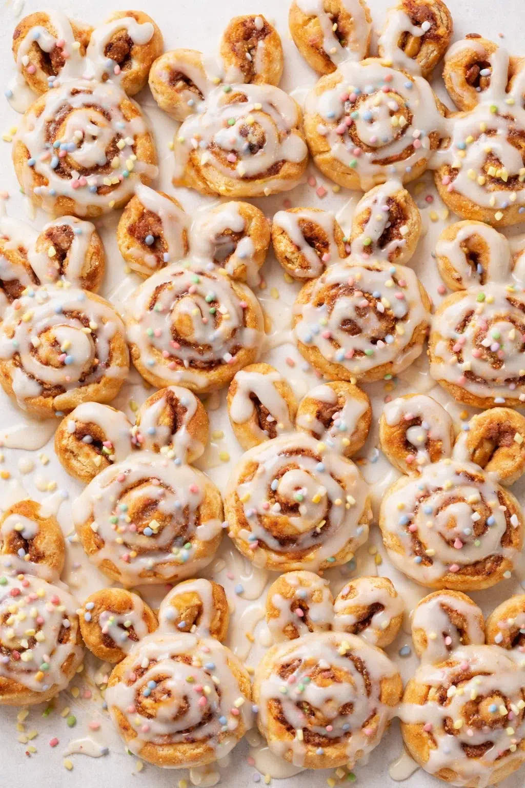 Overhead view of golden-brown cinnamon rolls with white icing and colorful sprinkles.