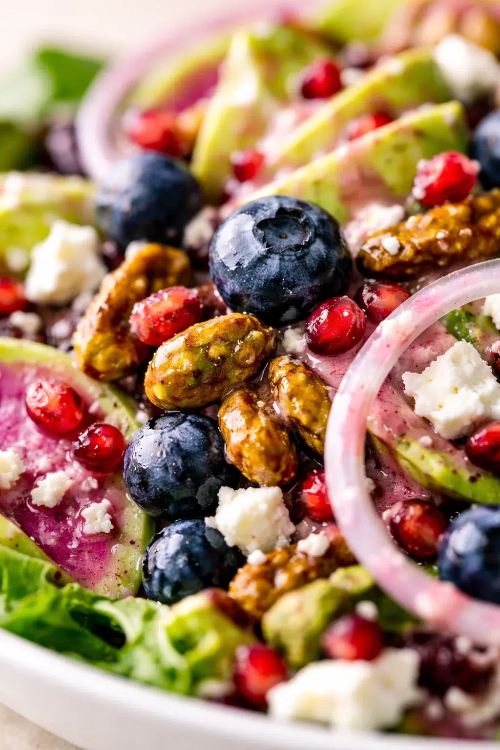 Close-up of a vibrant salad featuring blueberries, pomegranate seeds, candied nuts, watermelon radish slices, feta, and greens.