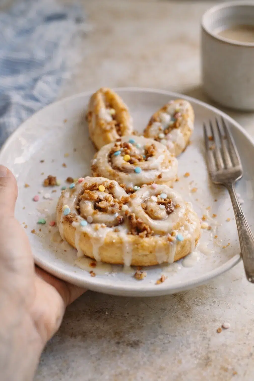 Creamy-iced cinnamon rolls on a white plate with pastel sprinkles and crumbs.