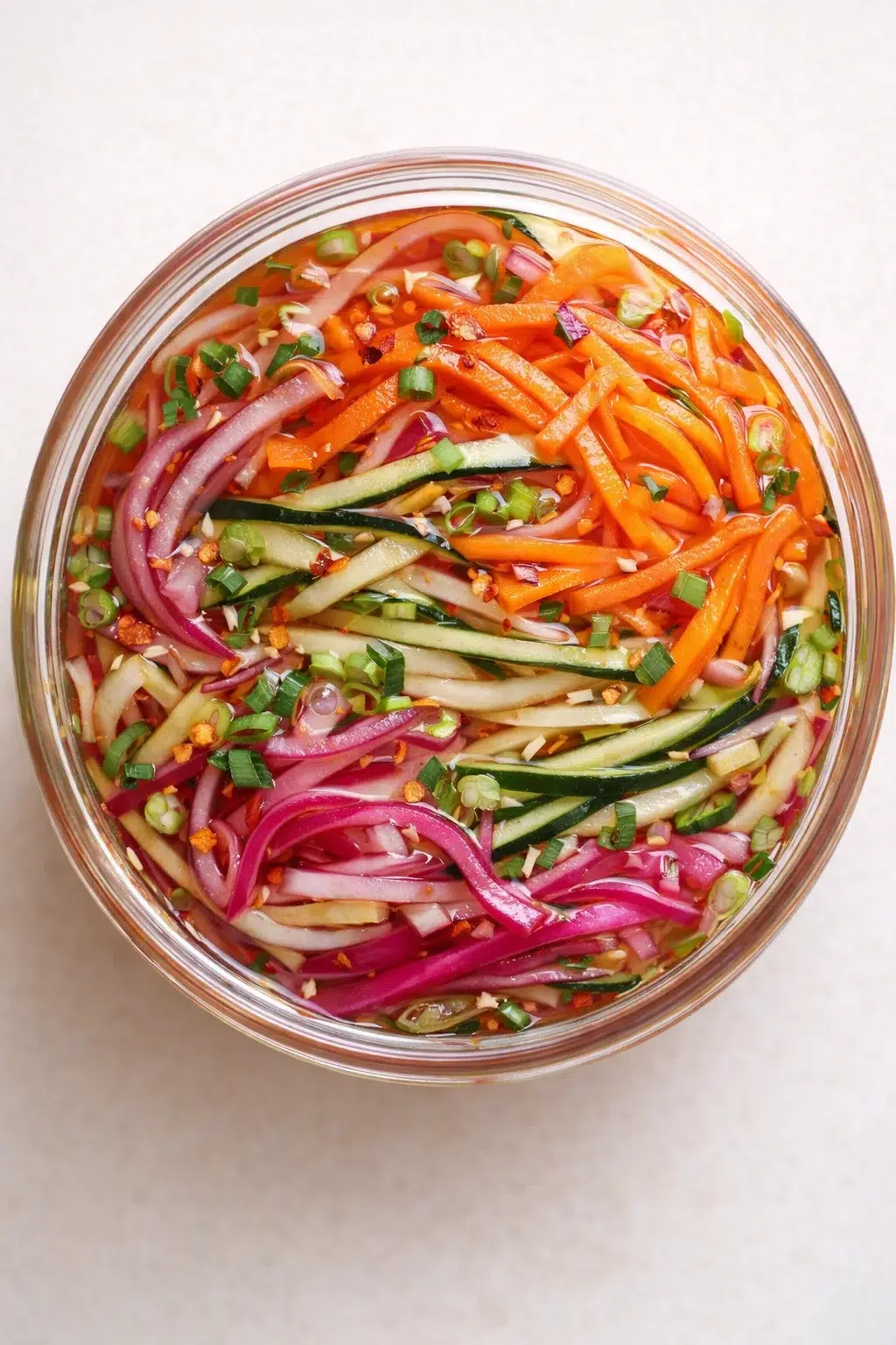 Top-down view of a glass jar brimming with colorful sliced vegetables in pickling liquid.