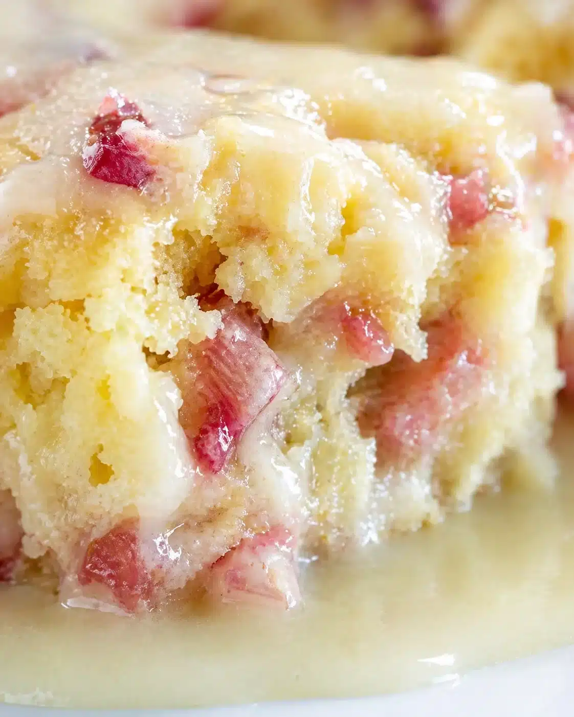 Close-up of a moist vanilla cake slice with pink fruit chunks and glossy glaze.