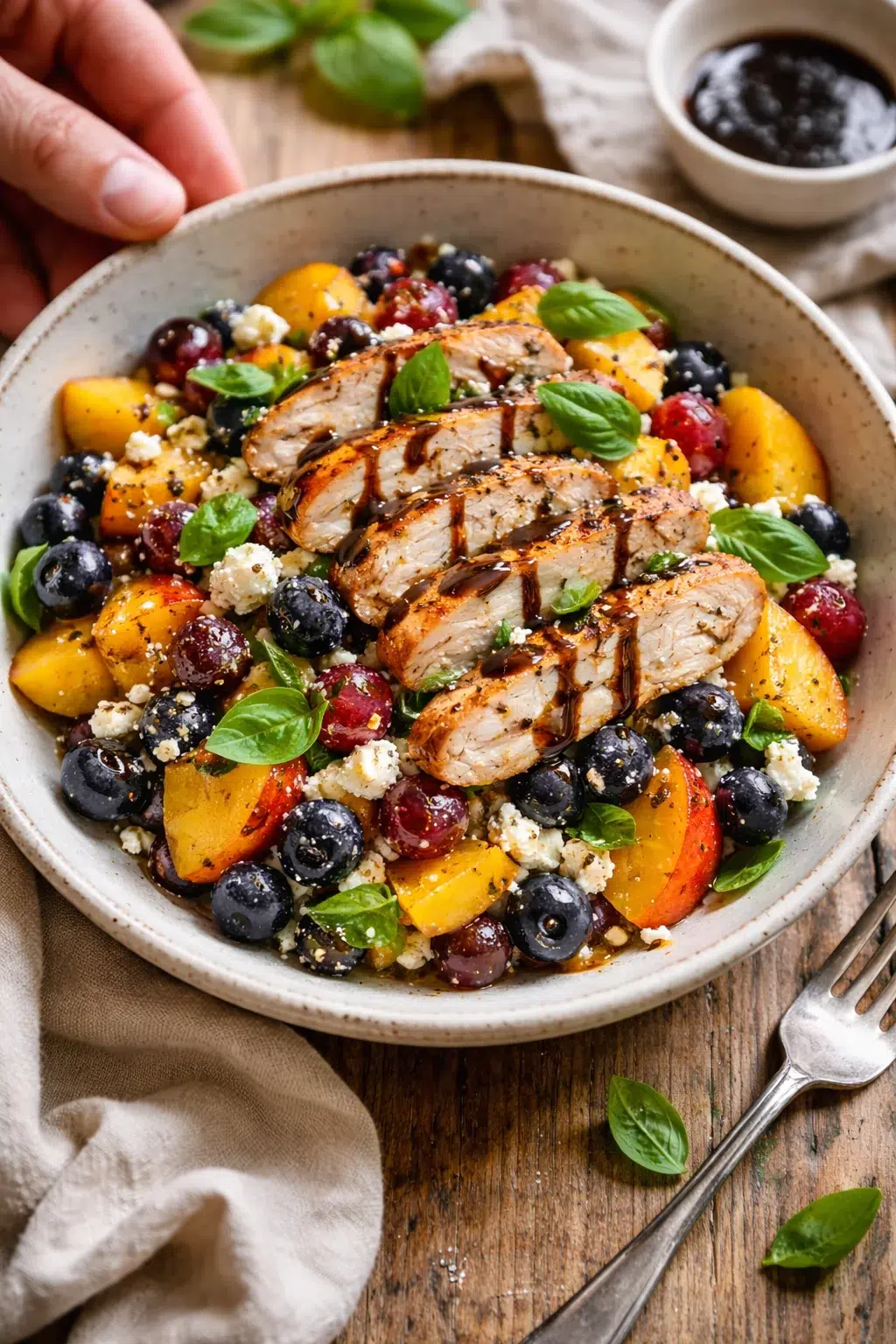 Sliced grilled chicken on a fruit medley with peaches, blueberries, grapes, feta and basil in a rustic bowl.