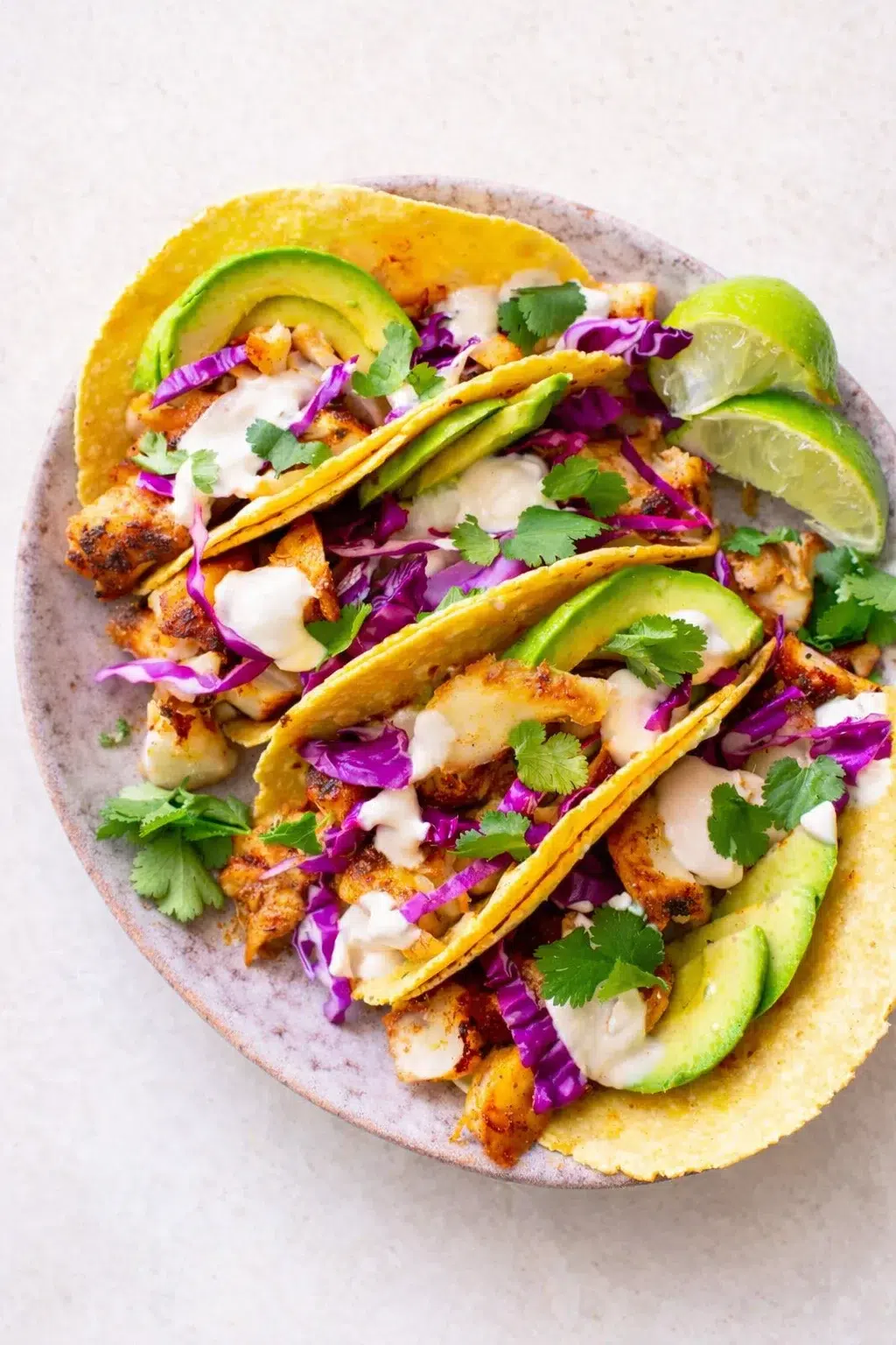 taco plate with grilled chicken, avocado, purple cabbage, cilantro, lime wedges, and crema on a ceramic plate.