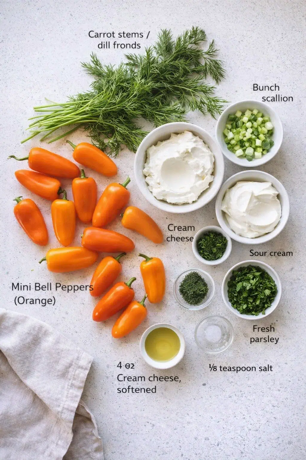 Overhead view of dill fronds, carrot stems, orange mini peppers, and bowls of cream cheese, sour cream, and chopped herbs for a dip.