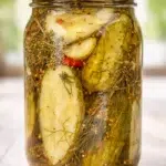 glass mason jar filled with cucumber pickles, dill, mustard seeds, and spices in brine.