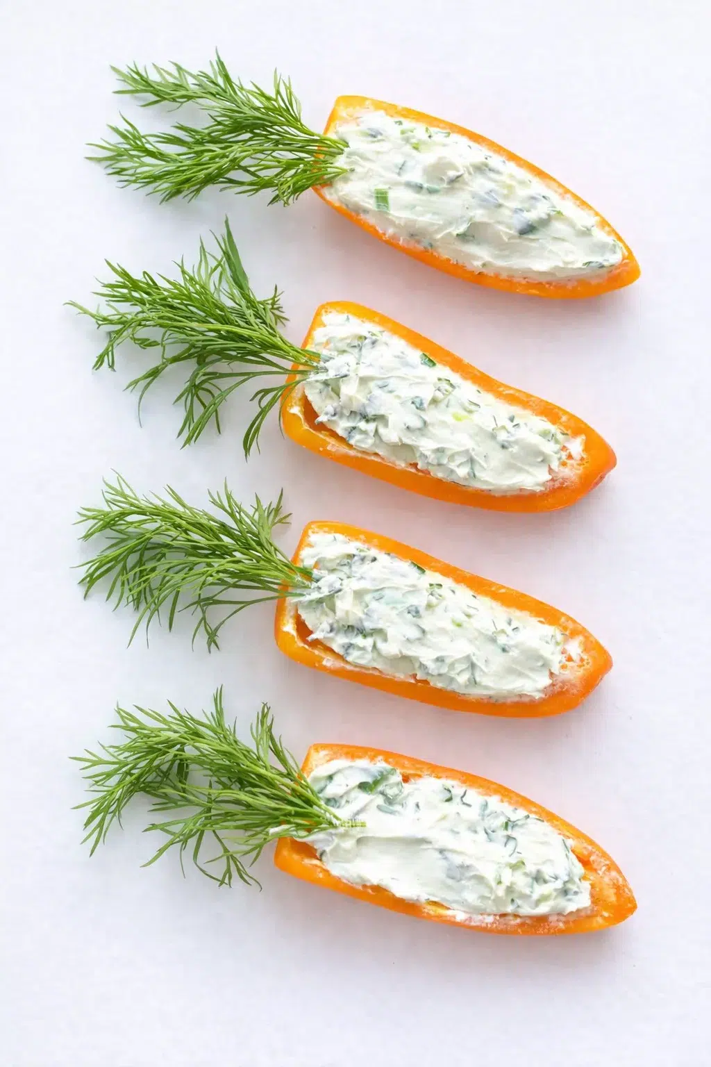Five orange pepper halves filled with creamy herb cheese and dill on a white background.