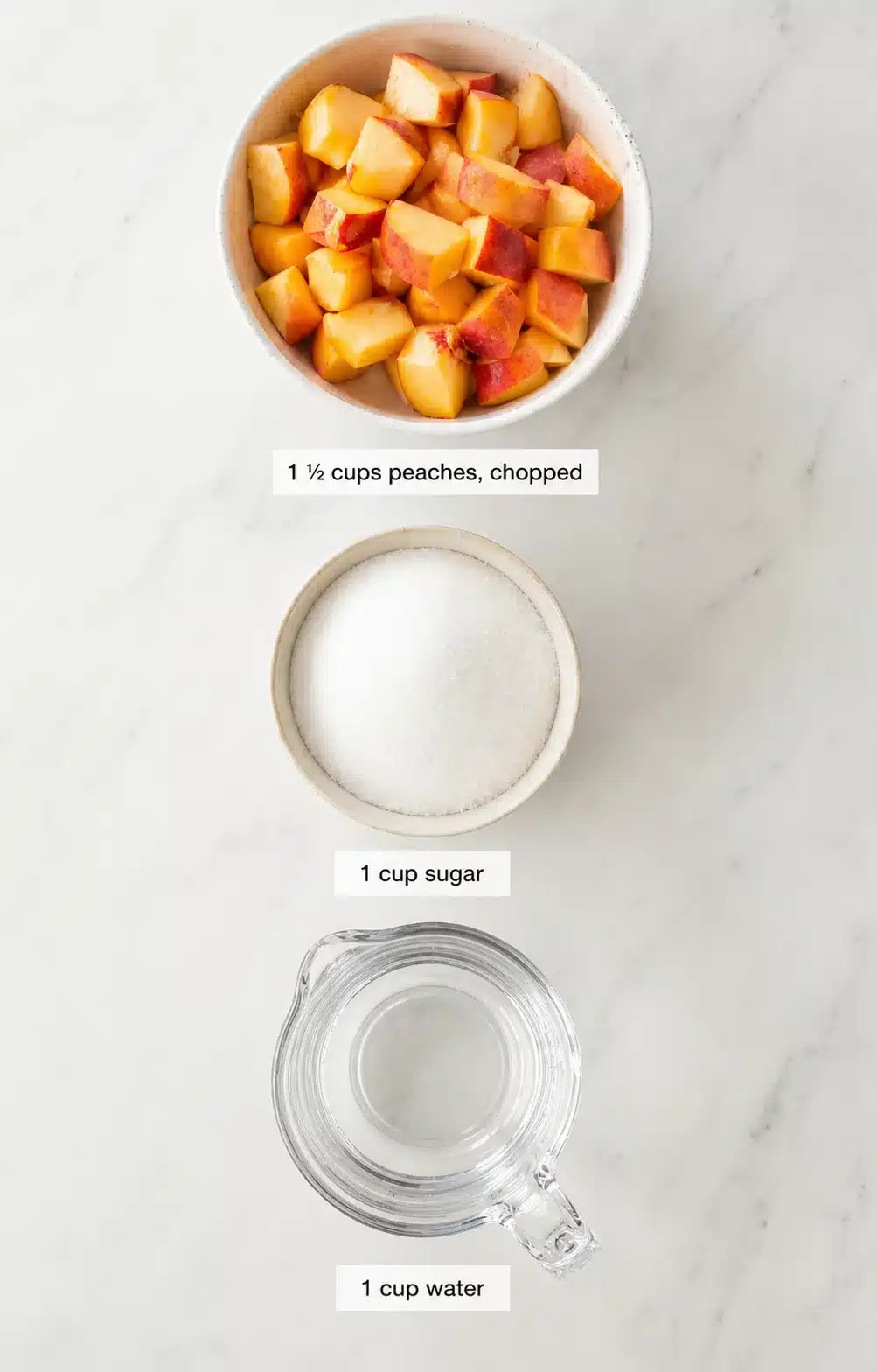 Overhead view of chopped peaches in a bowl, a sugar bowl, and a water measuring cup on marble.