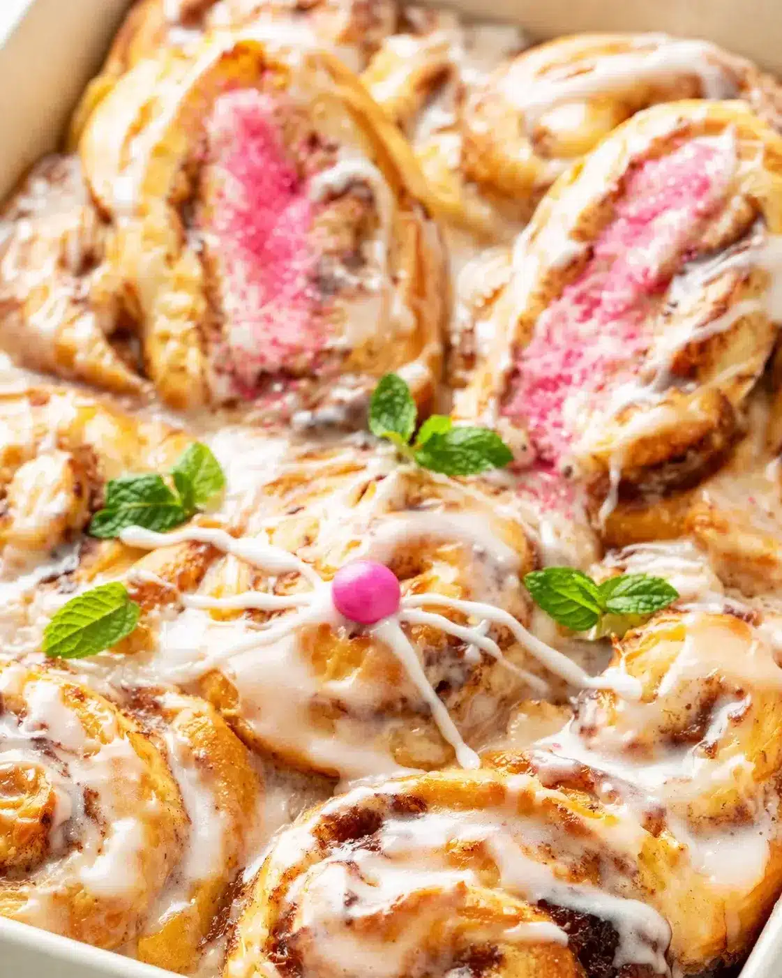 Cinnamon rolls with pink centers, white icing, and mint garnish in a baking dish.