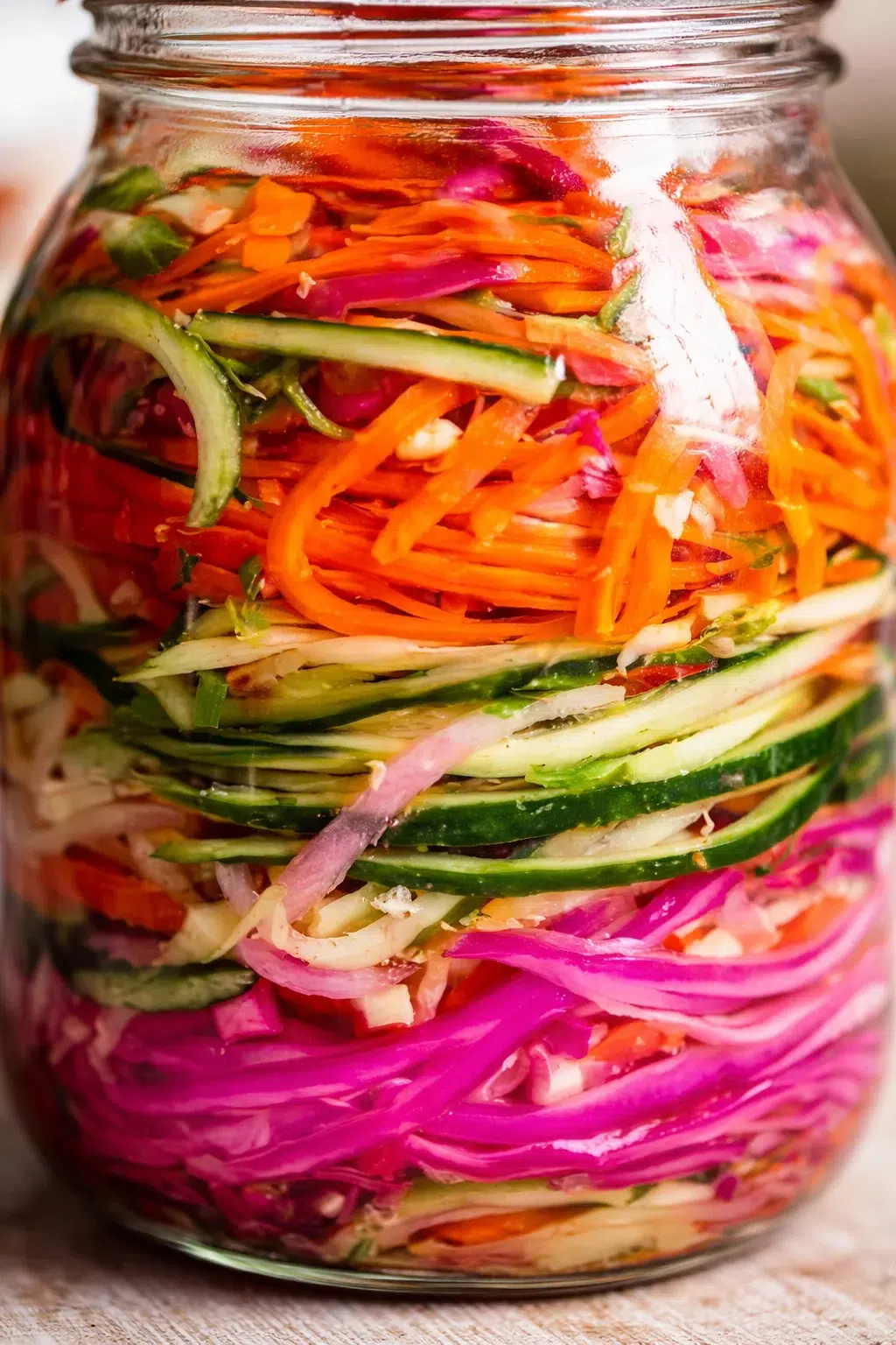 Colorful shredded vegetables layered in a glass jar for pickling