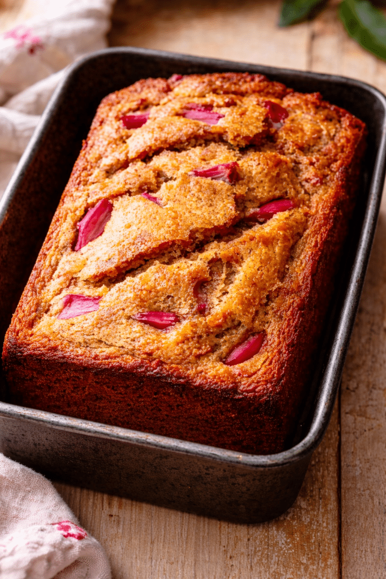 loaf pan with golden banana bread studded with pink rhubarb chunks and crumble topping