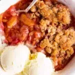 close up photo of rhubarb crisp in white bowl with vanilla ice cream