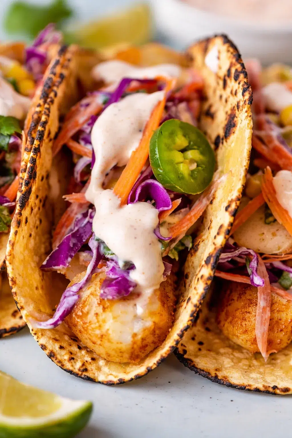 Two shrimp tacos on charred corn tortillas with purple cabbage slaw, jalapeño, and creamy sauce.