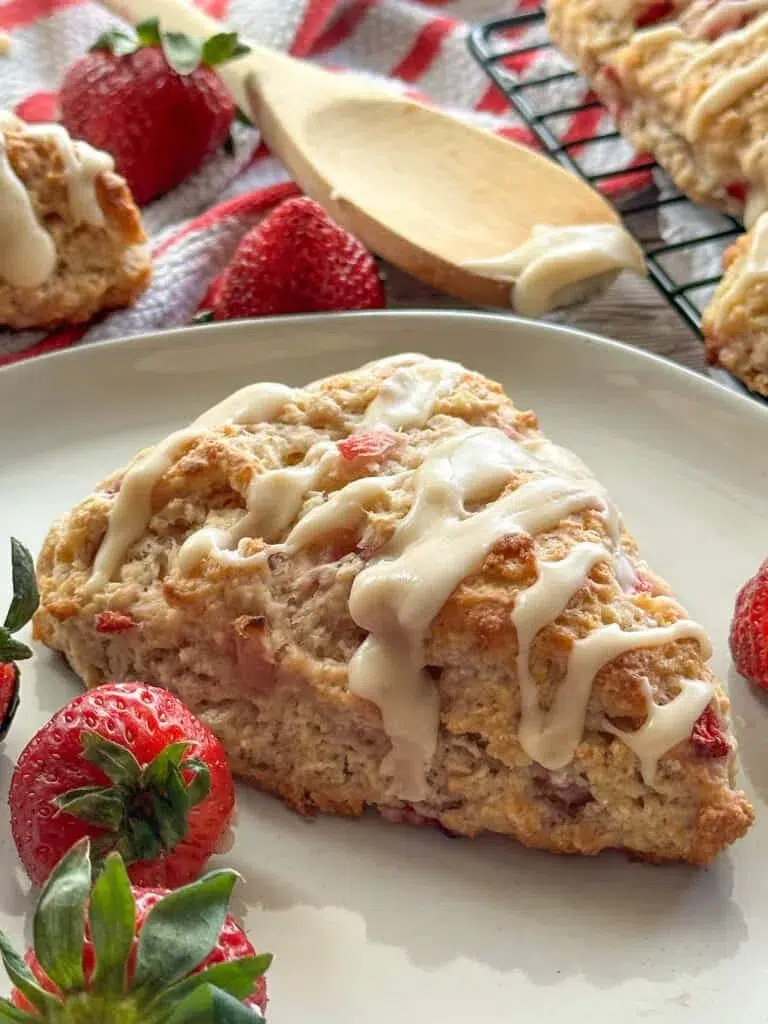 There is a sourdough strawberry scone that is glazed sitting on a plate with some strawberries.