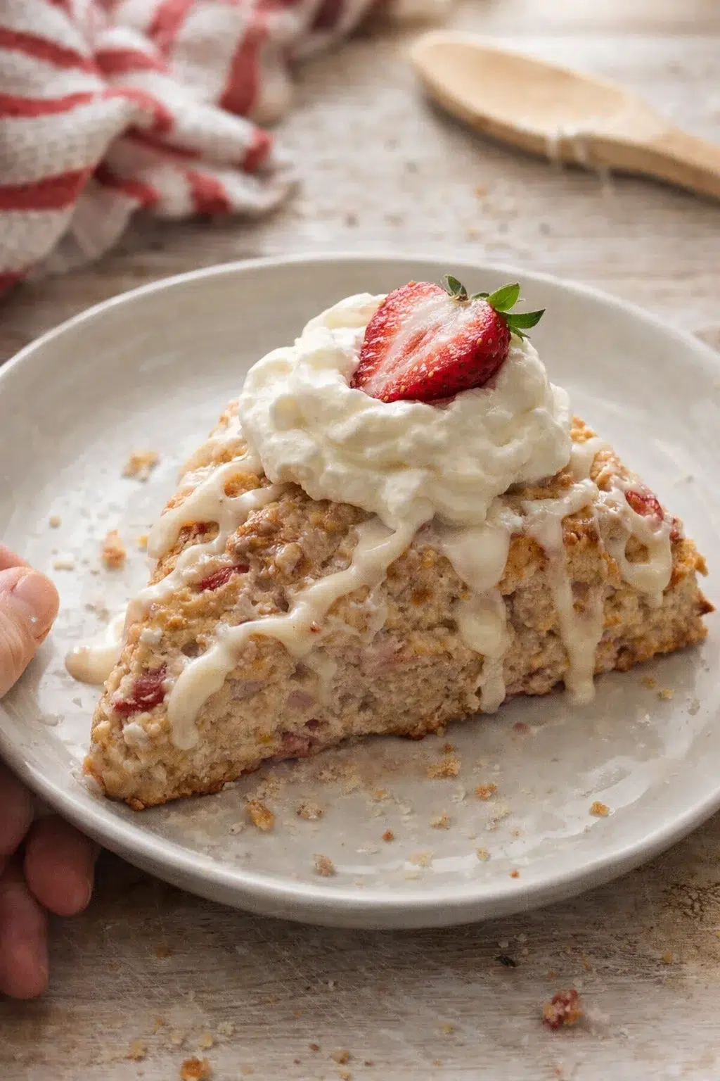slice of strawberry crumb cake with white glaze and whipped cream on a plate