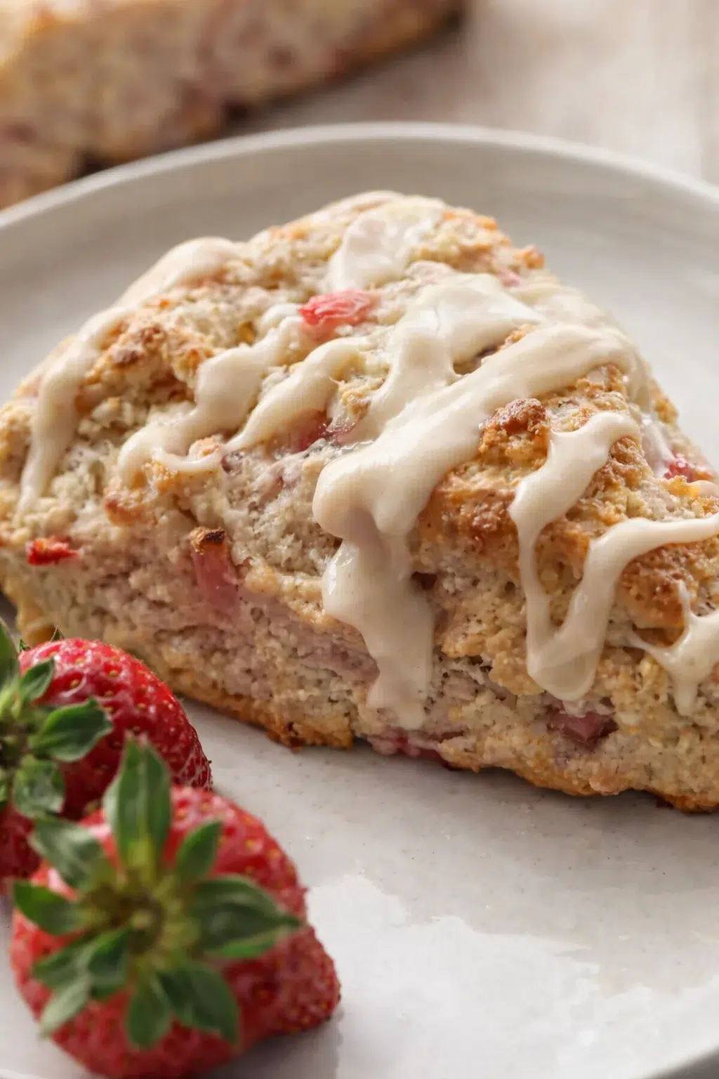 Close-up of strawberry-crumb quick bread slice with white icing on a light plate.