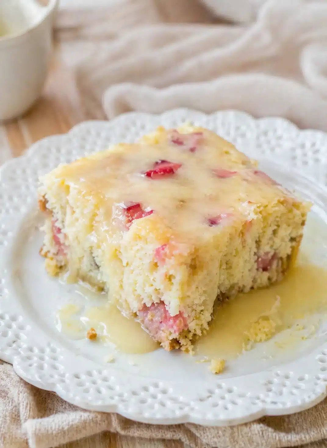 Thick vanilla cake slice with pink fruit chunks and pale glaze on a white plate.