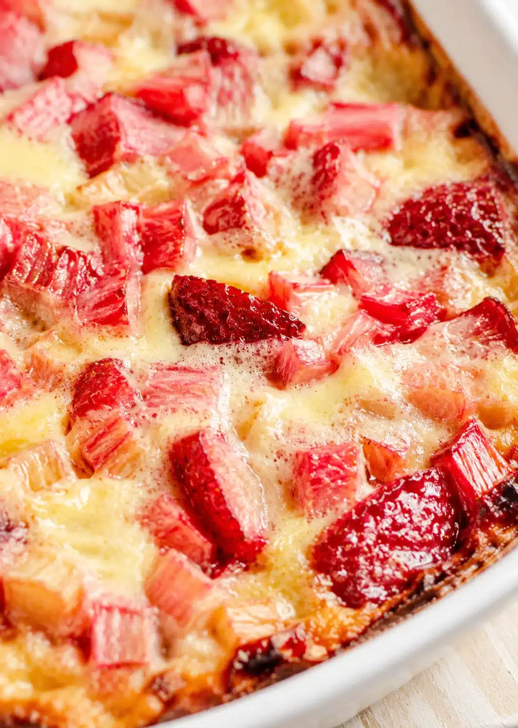 Close-up of a baked rhubarb dessert in a white dish, with red rhubarb chunks in creamy custard.