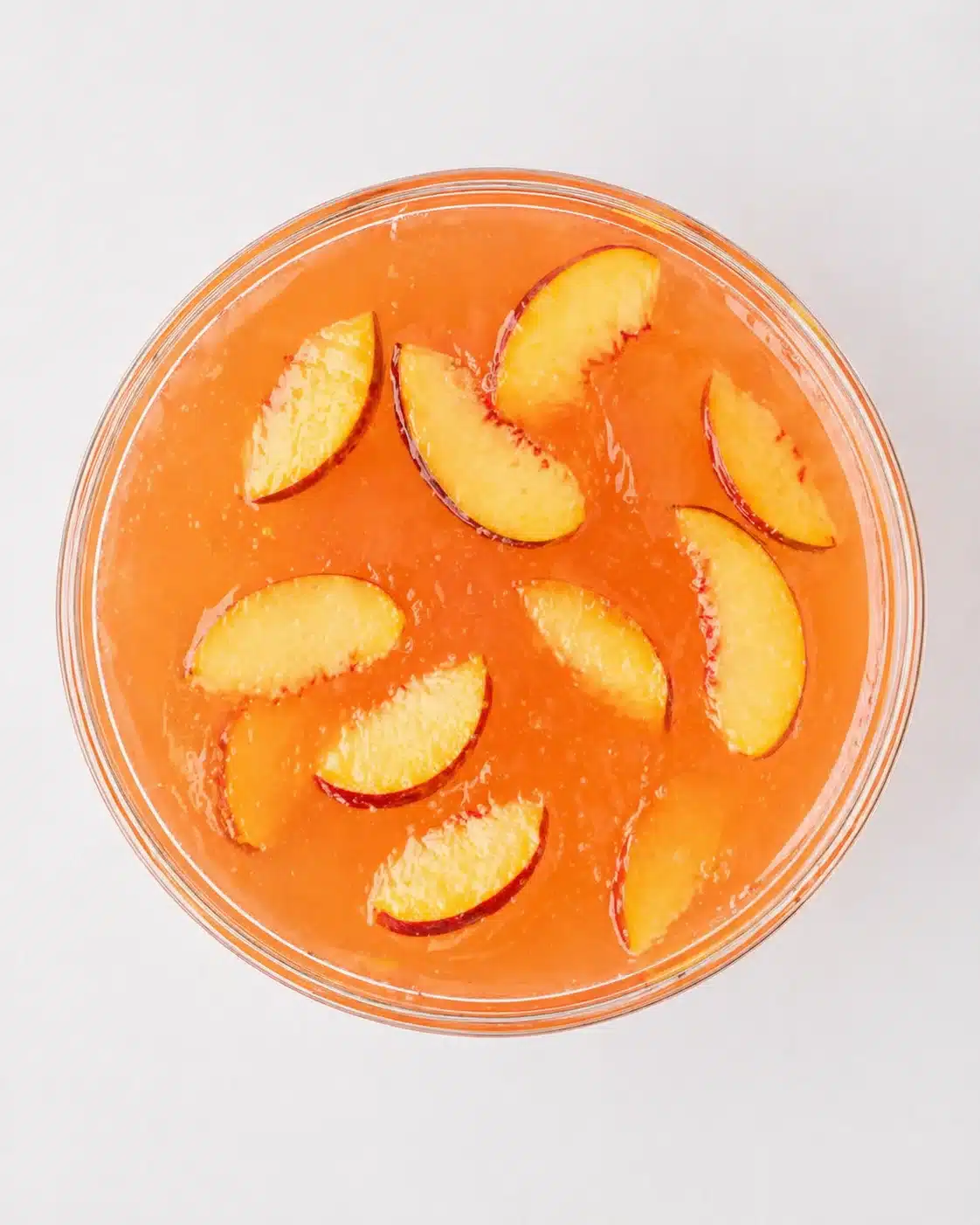 Top-down view of an orange beverage or dessert in a glass bowl topped with peach slices arranged around the surface.