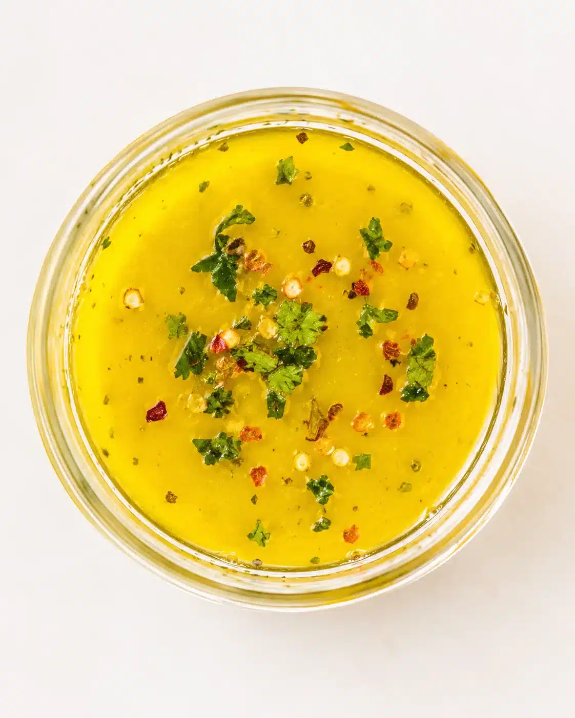Top-down view of bright yellow soup in a glass jar, garnished with cilantro and red chili flakes.