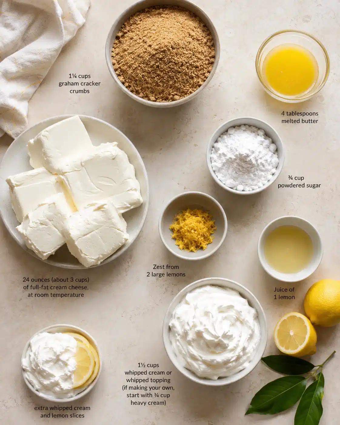 Top-down view of lemon cheesecake ingredients arranged with cream cheese, butter, sugar, crumbs, zest, juice, whipped cream.