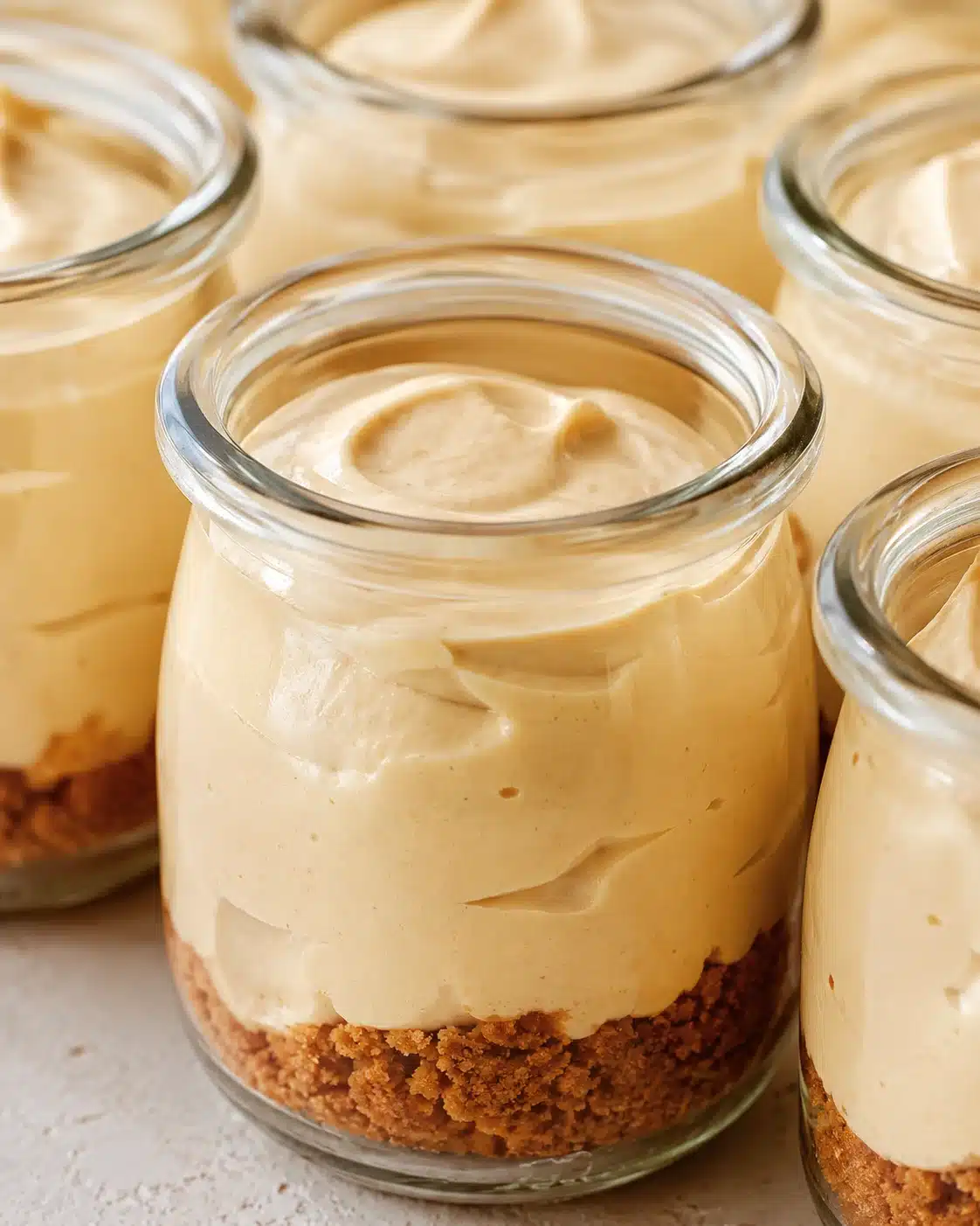 Close-up of creamy cheesecake filling in glass jars with a brown crumb crust.