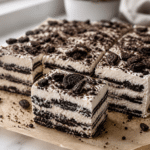 oreo icebox cake cut into squares with creamy whipped layers and chocolate cookie layers on parchment paper