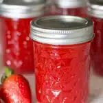 red strawberry jam in embossed mason jars with fresh strawberries nearby on a light surface